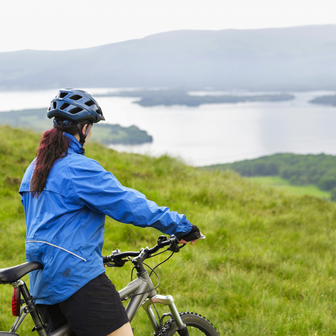 Woman in blue jacket wearing a helmet and on a bike on the Scottish Highlands.